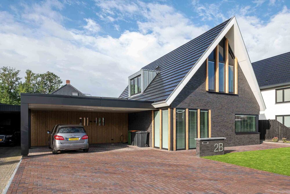 Nieuwbouwwoning met carport voor twee auto's. Grijs metselwerk met eikenhouten staanders.