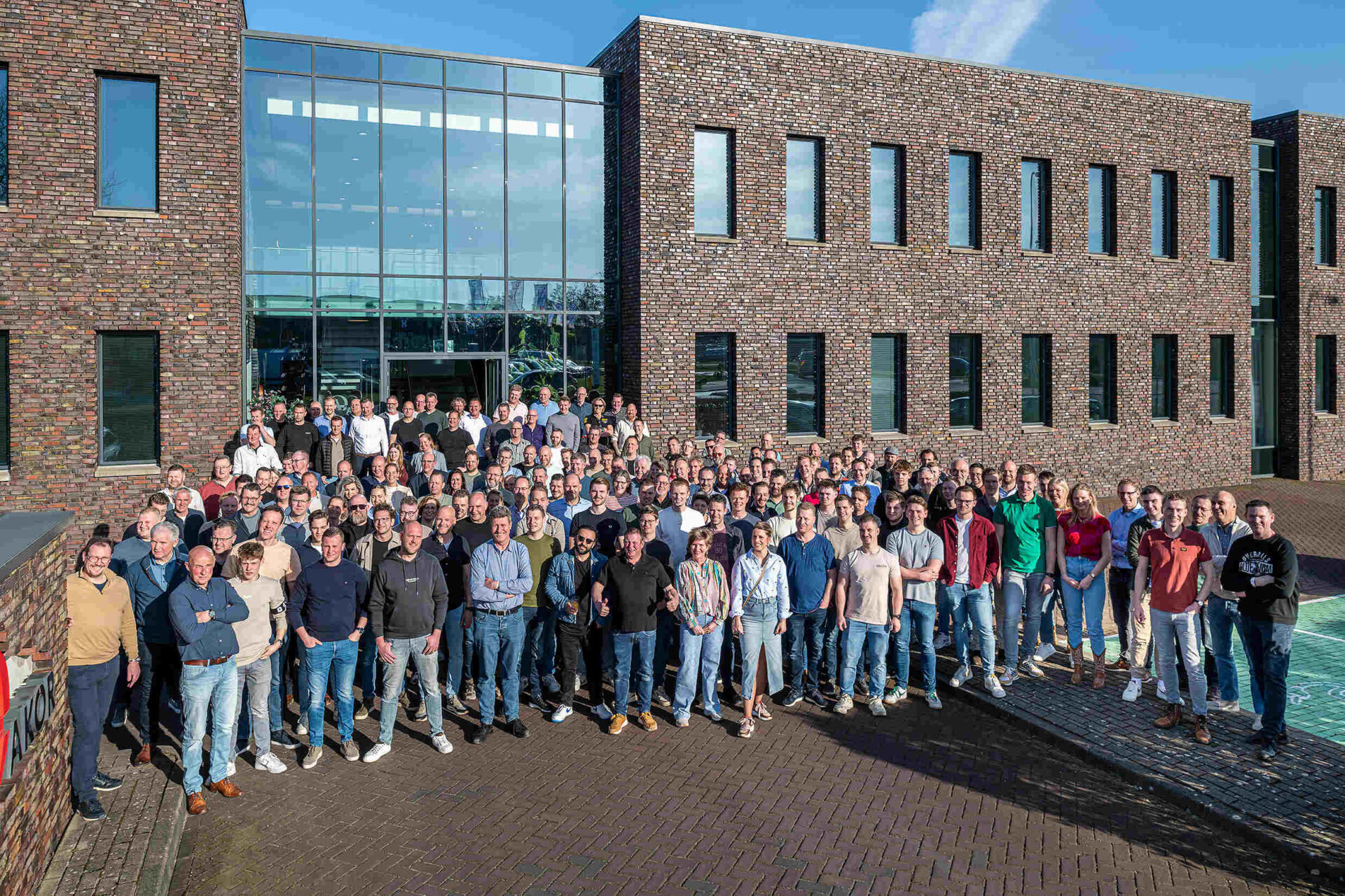 Teamfoto van AKOR voor het hoofdkantoor in Rijssen. Lekker met het hoofd in de zon.