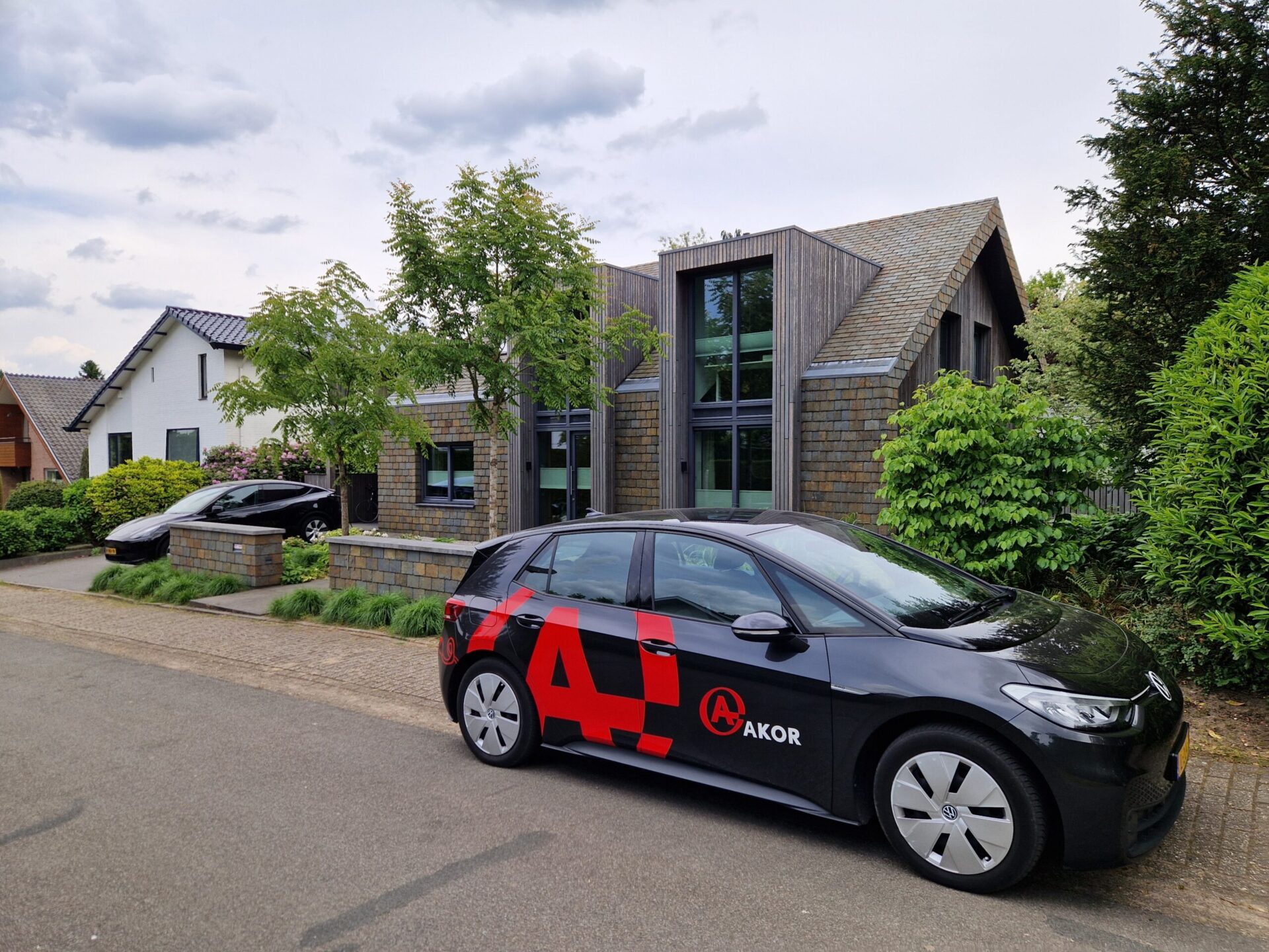 Minimalistische gevel met warme houtaccenten en robuuste leien bekleding. Deze woning in Schaarsbergen kreeg een complete transformatie met oog voor detail, materiaalgebruik en uitstraling. Een ID3 poolauto van AKOR voor de deur.